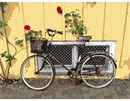 A charming bike with a basket leans against a yellow paneled wall.  Has a European touch.