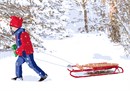 Boy sledding in the snow with a red coat and hat, green mittens, and blue shawl.